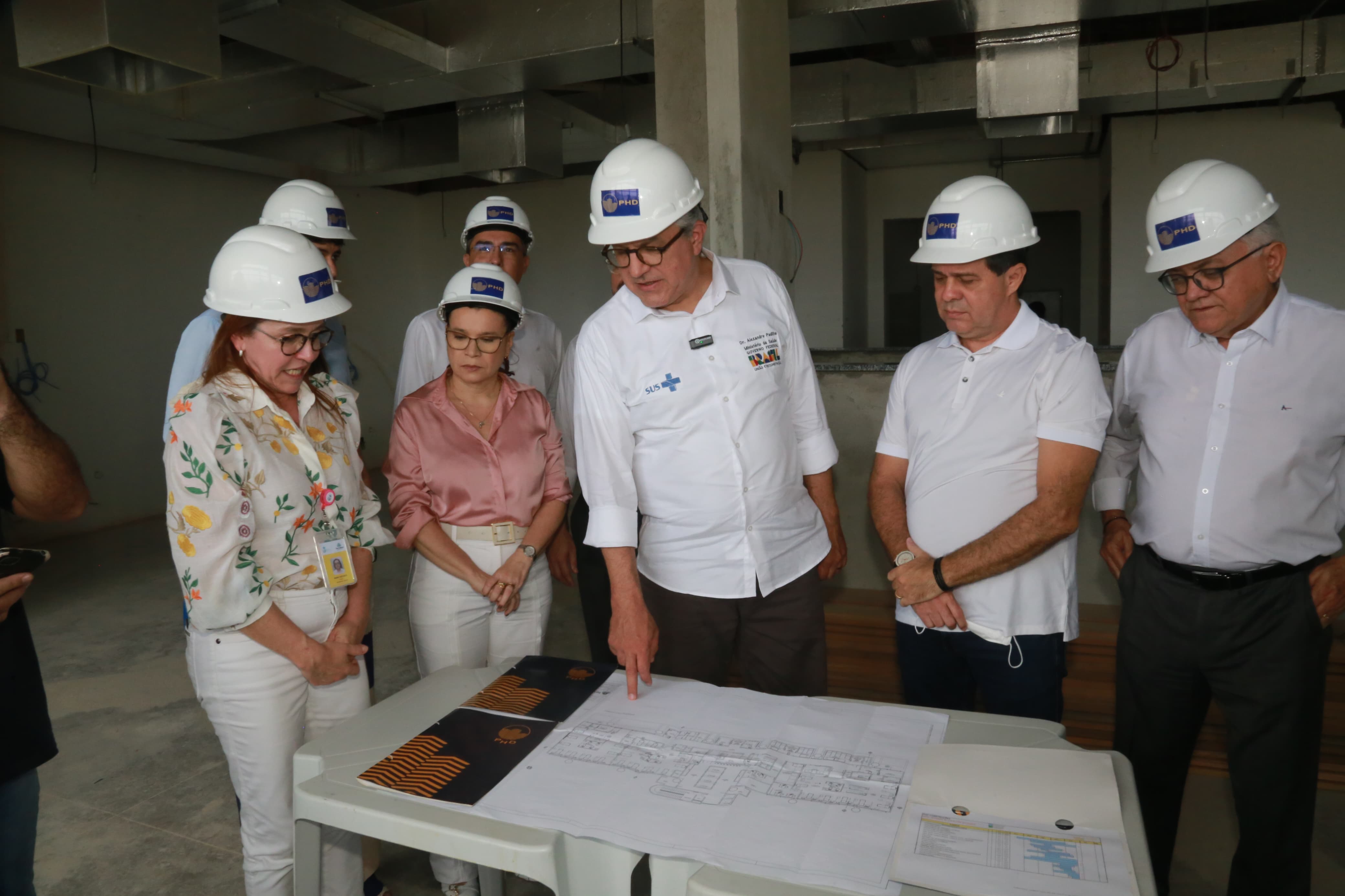 ministro Padilha e prefeito Evandro olham a planta baixa do IJF no canteiro de obras do hospital. Eles estão acompanhados de outras pessoas